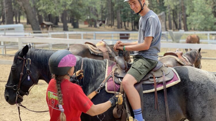 young man on black horse and a person helping guide him on the horse