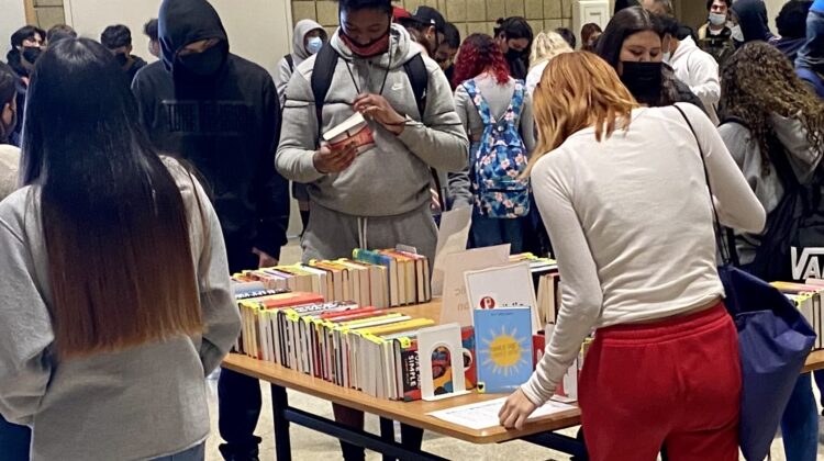 several teenagers looking at a table full of books